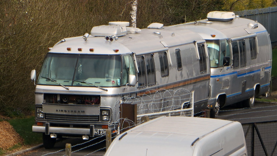 En silverfärgad Airstream husbil parkerad bakom ett metallstängsel med taggtråd. Fordonet har den karaktäristiska aluminiumexteriören.